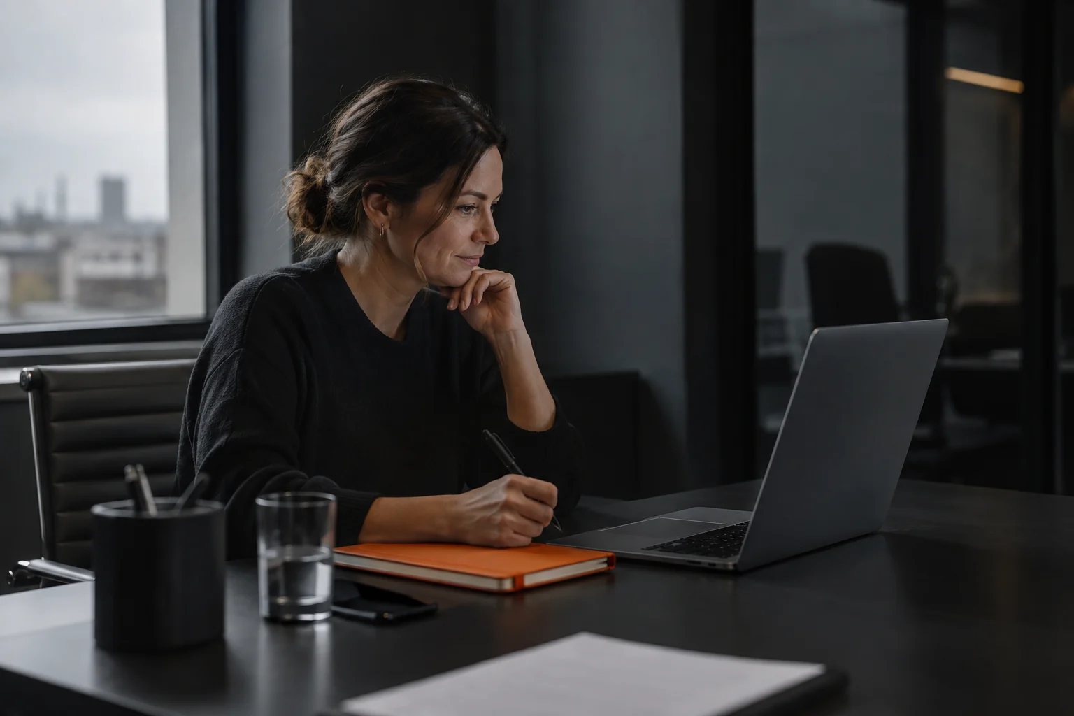 A woman listening on a video call with a notebook beside her laptop.